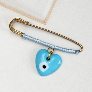 Detailed view of evil eye heart pendant with blue thread wrapping on gold brooch