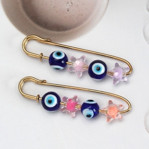 Macro detail of gold-tone safety pin brooches featuring evil eye beads and star charms
