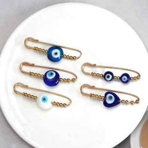 Close-up of golden Evil Eye safety pins with blue glass beads in a ceramic dish