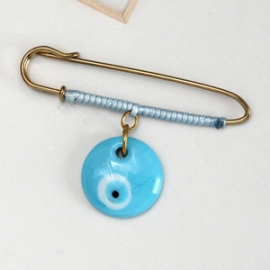 Detail of blue evil eye safety pin brooch with golden metal and thread wrap accent