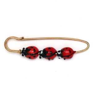 Golden safety pin brooch featuring three red and black enamel ladybug charms on white background