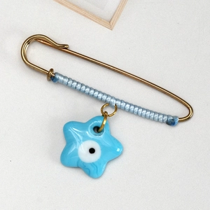 Detail of blue braided evil eye safety pin brooch with a star charm and gold finish