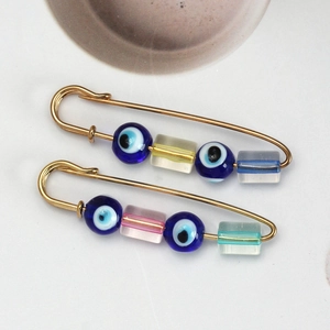 Detail view of two gold safety pin brooches featuring colorful glass beads and blue evil eyes