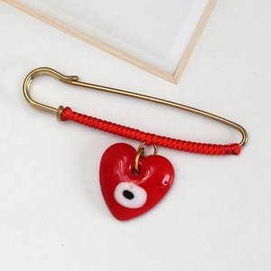 Detailed macro view of a gold safety pin brooch with red cord and evil eye heart charm