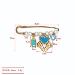 Détail d'une broche bébé dorée avec perles, œil protecteur et pendentif biberon vert menthe