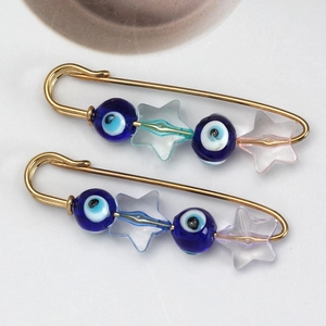 Detail of two gold safety pins with blue evil eye beads and frosted star charms