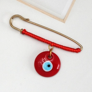 Detail shot of a red woven rope safety pin brooch with a glossy Evil Eye pendant charm