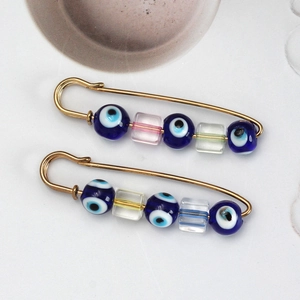Macro shot of two golden evil eye pins with colorful translucent glass square beads