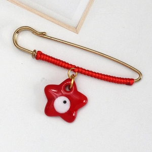 Close-up of golden safety pin with red braided rope and red star evil eye pendant