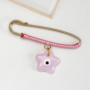 Detailed macro view of a pink braided safety pin brooch featuring a star evil eye charm