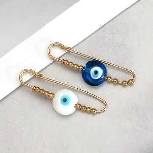 Set of two gold evil eye safety pin brooches with blue glass beads on textured background