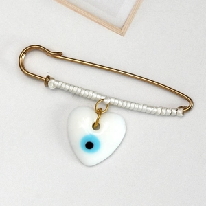 Detail of golden safety pin brooch with white silk wrap and heart evil eye pendant