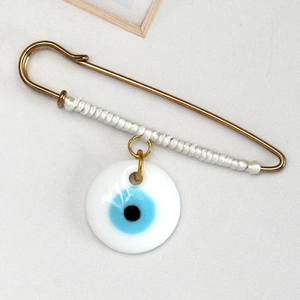 Detailed close-up of golden Evil Eye safety pin brooch with white thread wrapping