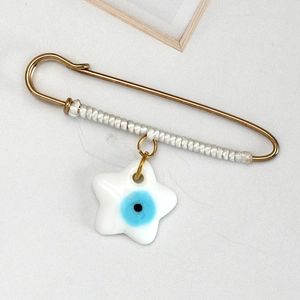 Detail of gold safety pin brooch with star evil eye pendant and white woven cord wrapping
