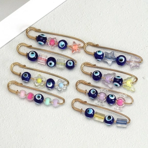 Detail view of gold safety pin brooches with evil eye beads and colorful charms