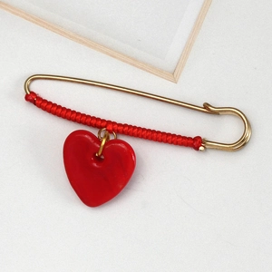 Detail of a large gold safety pin brooch with red braided rope and a red heart pendant