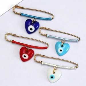 Detail of four colorful evil eye heart charms on gold safety pins with woven rope