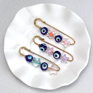 Three gold evil eye safety pins with colorful floral and star beads on a ceramic tray