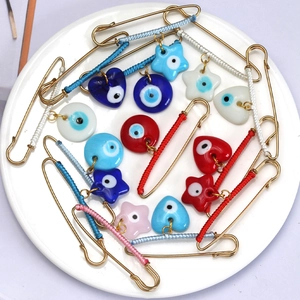 Macro shot of colorful woven silk threads and glass evil eye charms on golden safety pins