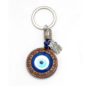 Close-up of blue glass evil eye keychain with silver owl charm and wooden base