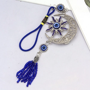 Détail d'une suspension murale œil grec bohème avec charmes soleil lune et pompons bleus