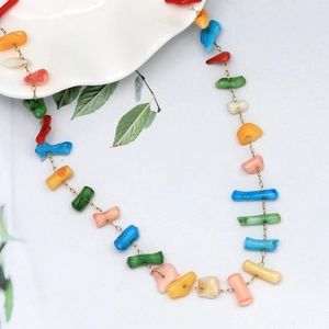 Collier artisanal de perles en pierres naturelles colorées avec chaîne dorée sur plat blanc