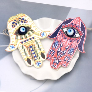 Detail of Hamsa Hand keychains with blue Evil Eye beads on white ceramic plate