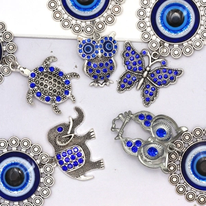 Flat lay showing elephant, owl and turtle evil eye charms with blue rhinestones and silver finish