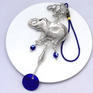Detailed view of silver elephant pendant with blue evil eye beads on white ceramic tray
