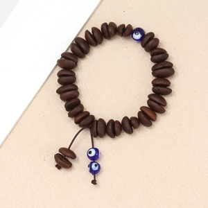 Detail of coffee bean beaded bracelet with blue evil eye charms on a beige surface