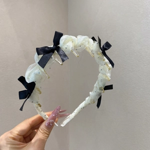 Détail d'un serre-tête en résille blanche avec nœud noir, strass et peigne intérieur