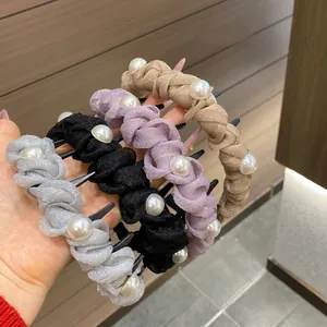 Detailed view of woven pearl hair clips in four elegant colors held by hand