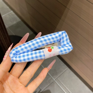 Détail d'une pince à cheveux à carreaux bleus avec broderie cerise et texture éponge