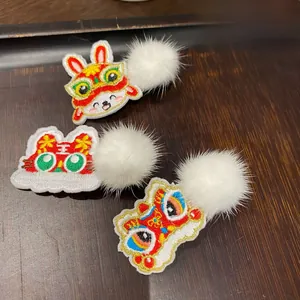 Detail of Chinese style embroidered hair clips with festive lion patterns and white pom-poms