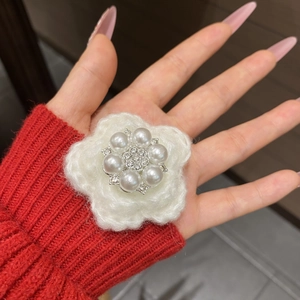 Macro detail of a white knitted flower clip featuring central pearl and rhinestone accents