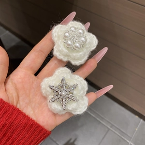 Detailed view of handmade plush white knit snowflake hair clips with pearl flower accents