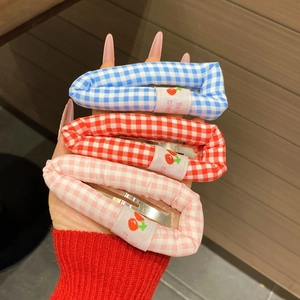 Gros plan sur trois barrettes à cheveux à carreaux bleu, rouge et rose avec étiquette cerise