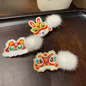Detail of embroidered New Year hair clips with traditional lion and bunny patterns and white pom-poms