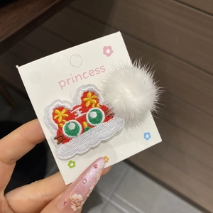 Detail view of Chinese New Year hair clip with lion dance embroidery and white pompom