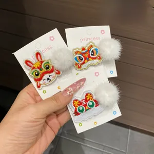 Detailed view of three Chinese New Year hair clips with lion dance embroidery and white pom-poms