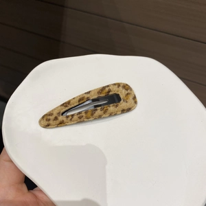 Close-up of a leopard print plush teardrop hair clip held over a white ceramic tray