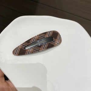 Detail view of a vintage brown plaid fabric BB clip on a white ceramic tray