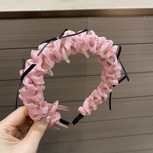 Détail d'un serre-tête en tissu plissé rose avec nœud noir et dents intérieures antidérapantes