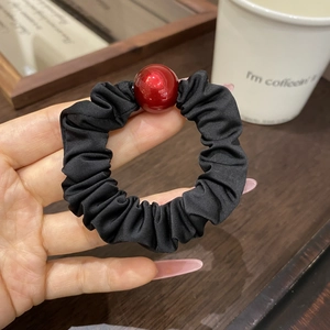 Close-up of black pleated fabric hair tie with a glossy red bead on a person's wrist
