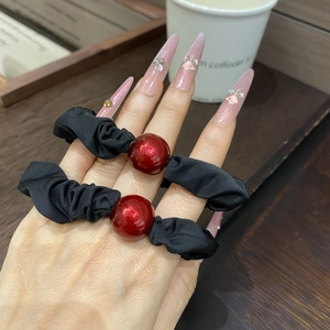 Close-up of black satin hair scrunchies with large red beads on a person wrist