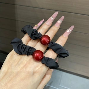 Detail of black fabric hair ties featuring glossy red beads worn on a person's hand