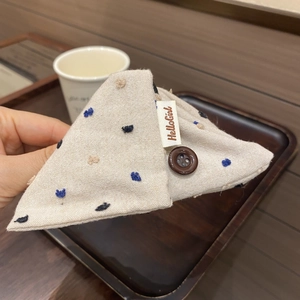 Détail de la pince à cheveux en lin beige avec broderie bleue et bouton marron poli
