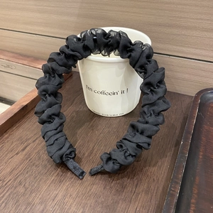 Detail eines schwarzen plissierten Haarreifs im Scrunchie-Stil auf einem weißen Becher