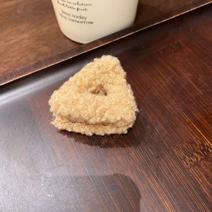 Dettaglio di un fermaglio a triangolo in peluche beige su un vassoio di legno