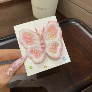Détail de la broderie d'une pince à cheveux papillon rose et blanche avec fil doré